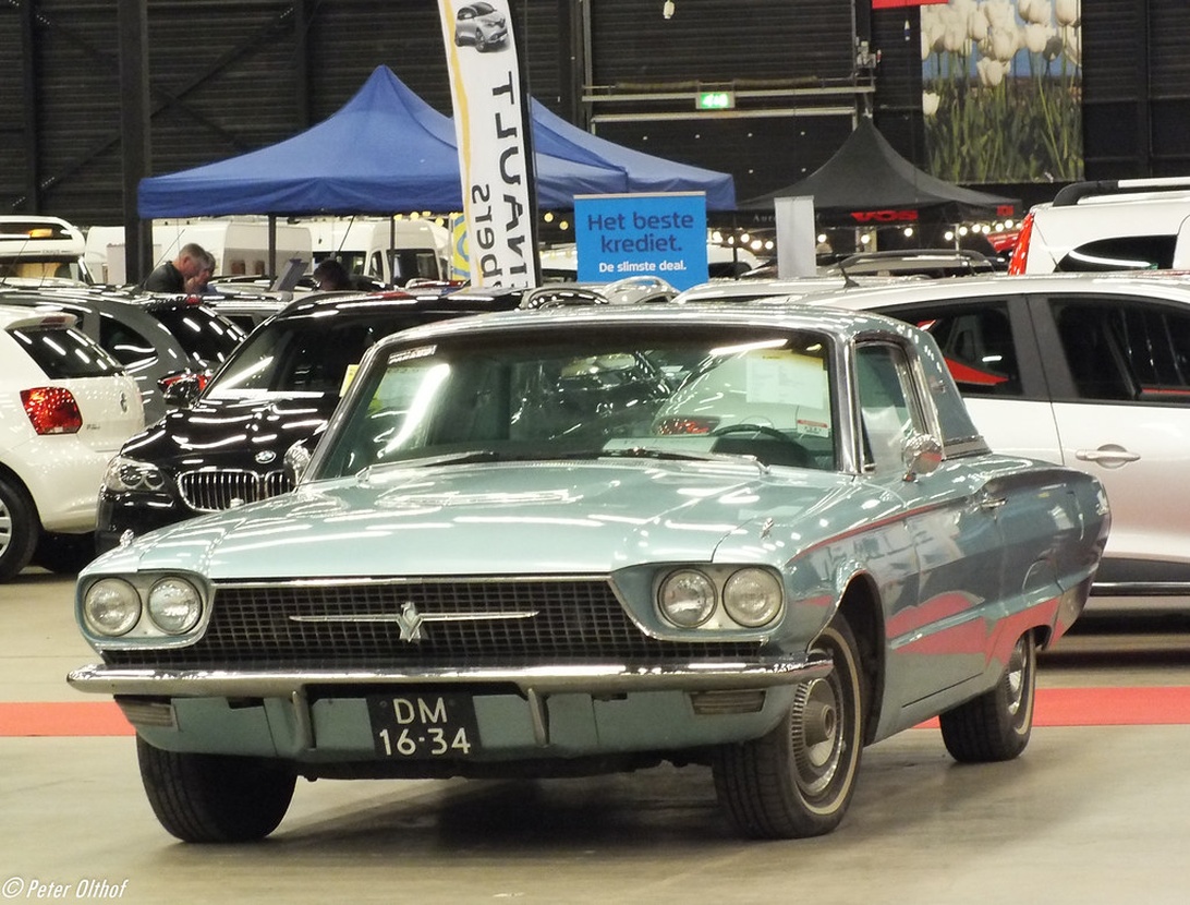 En ljusblå klassisk amerikansk bil, troligen en Ford Thunderbird från 1960-talet, på en stor inomhusauktion i Europa.