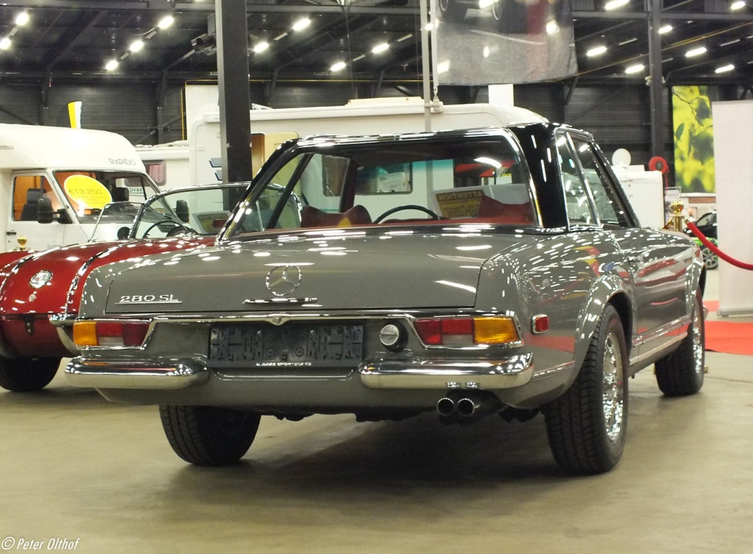 Bakifrån av en klassisk Mercedes-Benz 280SL i silvergrått, utställd på en inomhusauktion på en röd matta.